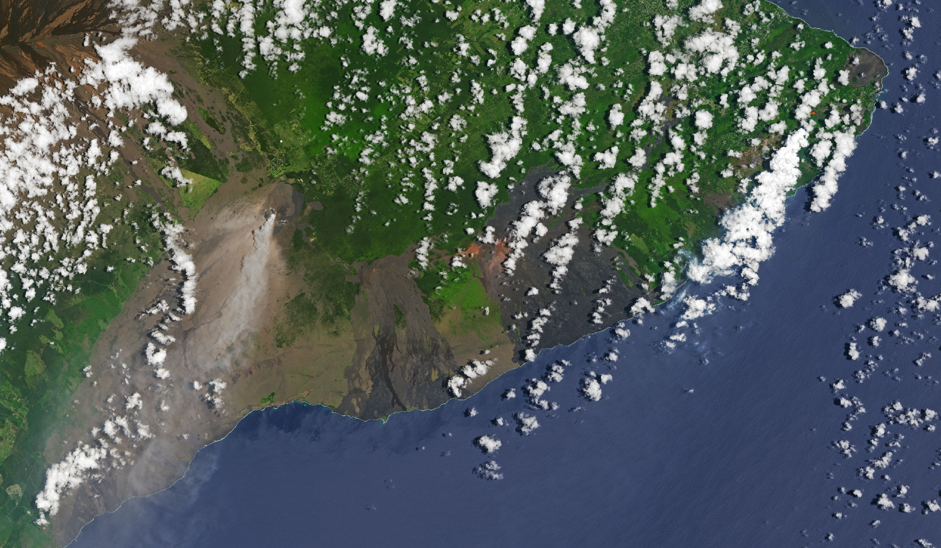 Satellite image of Kilauea volcano in Hawaii.  The island containing the volcano is a mix of green and brown, and it has a perimeter going from the bottom left of the image to the top right of the image. Outside of that perimeter is water, which has a blue color. Shadows are cast on the land and water by clouds, which have a white color, that float above.