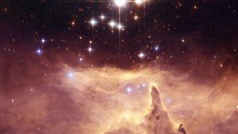 Pinkish gas and dust with spire-like pillar below a small loose cluster of stars.