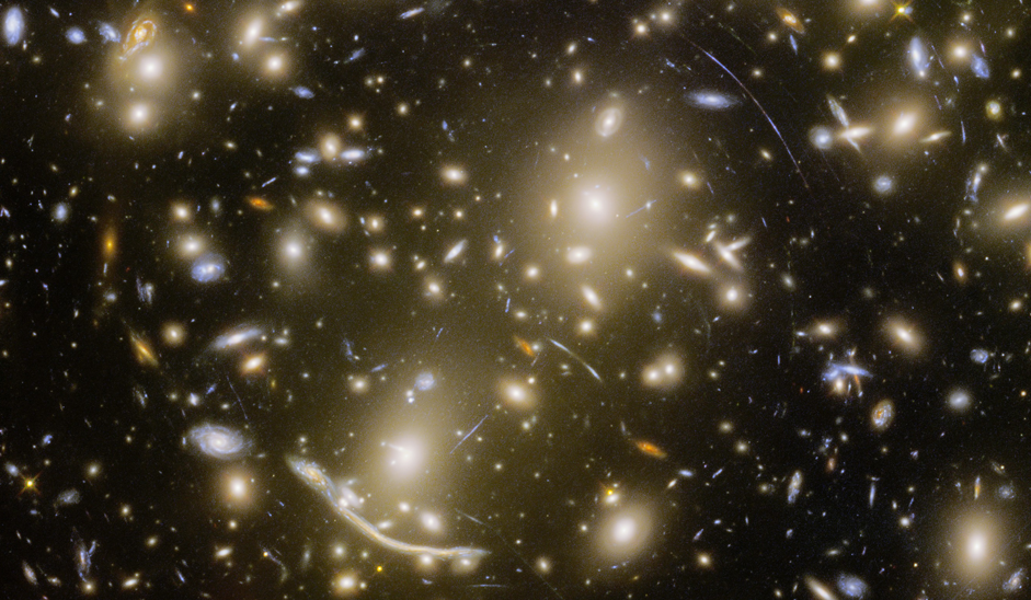 Many bright white, yellow, orange and blue galaxies of different shapes and sizes. Several of these galaxies have arc-like shapes.