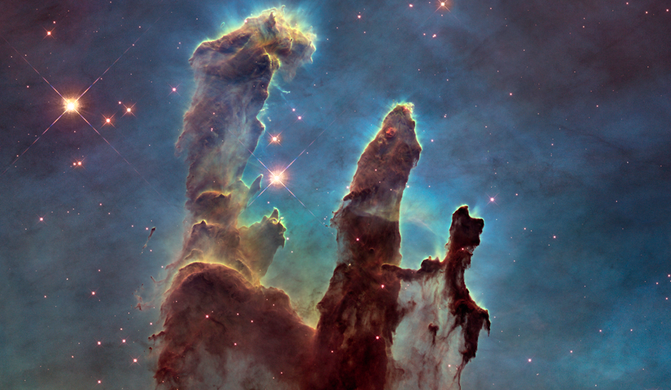 Pillars of gas and dust. Toward the center of the image are three dark brown pillars that rise from the bottom to the top of the screen. The leftmost pillar is the tallest, the rightmost pillar is the shortest, and the middle one is in-between left and right in size. Surrounding each pillar is an aura of glowing, yellow gas. The background is opaque, blue and purple at the top, and contains handful of red stars of various sizes.