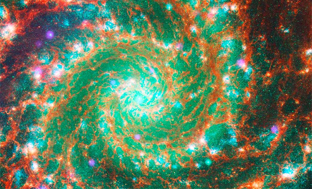 Color composite of the mid-infrared, visible, ultraviolet, and X-ray light from the spiral galaxy M74 (the Phantom Galaxy). The perspective and field of view are the same as in all of the other images. Each form of light is shown in a different color. The mid-infrared light captured by the James Webb Space Telescope is shown as red. The red is concentrated in the dust lanes and veins along and between the spiral arms. The visible wavelengths of light from the Hubble Space Telescope are shown as green. The green is most prominent in the points of starlight between the veins of dust within and between the arms. The ultraviolet wavelengths of light collected by XMM-Newton are shown as blue. The blue is most apparent in the fuzzy clumps along the spiral arms. The bands of X-ray light from the Chandra X-ray Observatory are shown as purple. Glowing orbs of purple are scattered here and there along and between the arms. The bright colors and the very distinct and complex spiral pattern combine to give the image a psychedelic feel. The image is brightest at the center. The brightness decreases and overall contrast increases with distance from the center. Most of the structures that are visible in the individual images are also visible in this composite. Some structures, like the orange-brown lanes of dust and the bubbles between the veins of dust, are very pronounced. Others, like the red knots that glow in visible and infrared, the blueish clumps of ultraviolet light, and the purple sources of X-ray light overlap and are harder to differentiate.