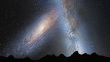 Illustration of two galaxies (Milky Way and Andromeda) colliding in the sky above  the silhouette of a mountain range.