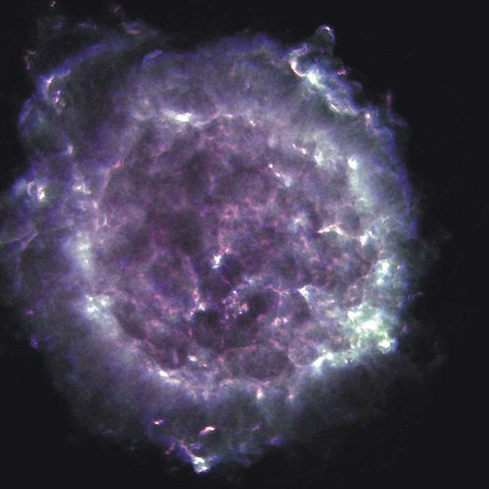 The Cassiopeia A supernova remnant appears as a luminous, roughly circular cloud with a mix of purple and white colors against the dark backdrop of space. The interior appears mottled with dark and bright filaments. Faint glimmers of white around the edges highlight its spherical shape.