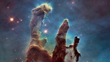 Image of the Pillars of Creation showing three dark brown towers against a light blue background scattered with stars.