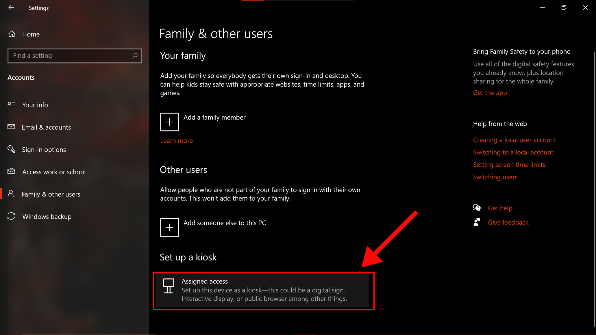 Screenshot of the Windows “Family and other users” window. Toward the bottom, underneath the “Set up a kiosk” section, a large red arrow points to the "Assigned access" option, which is highlighted by a red rectangle.