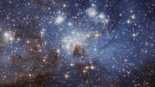 A field of stars of different sizes and brightness with some dark brown clouds, all on a background of deep blues.